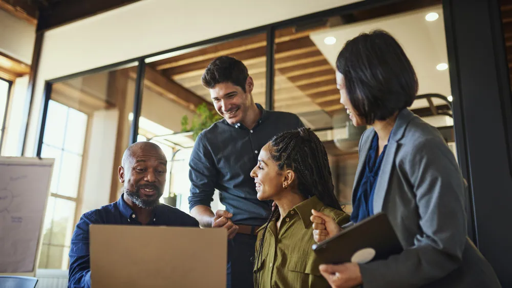 ALT Text: Project manager and teammates smiling cheerfully at team meeting in boardroom, excited over business plans on laptop